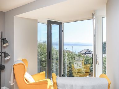 A room with yellow armchairs near open glass doors overlooking houses and a body of water at Cambrian House in Criccieth