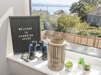 A windowsill with a welcome sign binoculars a lantern and small potted plants at Cambrian House in Criccieth