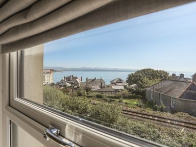 View of houses trees railway tracks and sea through a window at Cambrian House in Criccieth