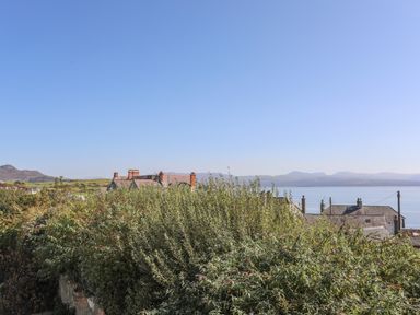 A view of a coastal village with houses surrounded by dense vegetation and hills in the background at Cambrian House in Criccieth
