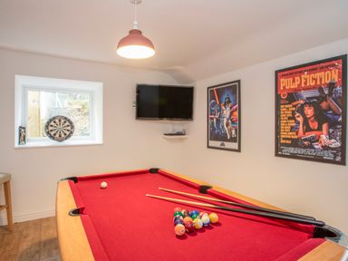 A game room with a red pool table darts board on a windowsill and a wall-mounted television at Cambrian House in Criccieth