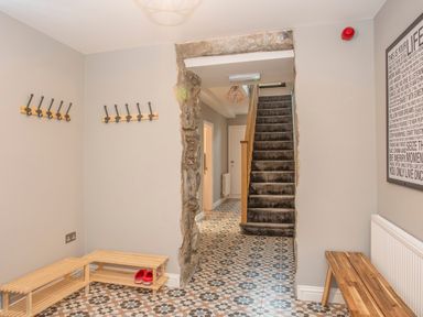 A hallway with patterned floor tiles wooden benches wall hooks and carpeted stairs at Cambrian House in Criccieth