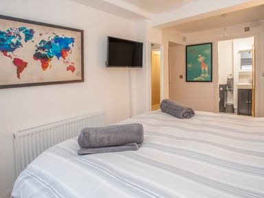 A bedroom with a bed with striped bedding and rolled towels a wall-mounted tv and colorful world map artwork at Cambrian House in Criccieth