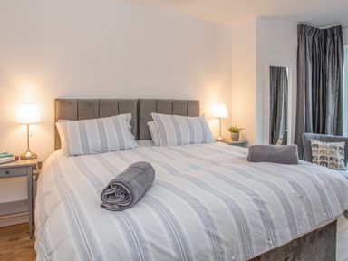A bedroom with a large bed with striped bedding two bedside tables with lamps and a chair with cushions at Cambrian House in Criccieth