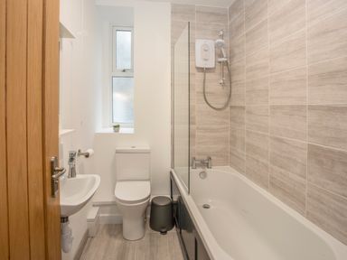 A bathroom with a bathtub shower toilet and sink at Cambrian House in Criccieth
