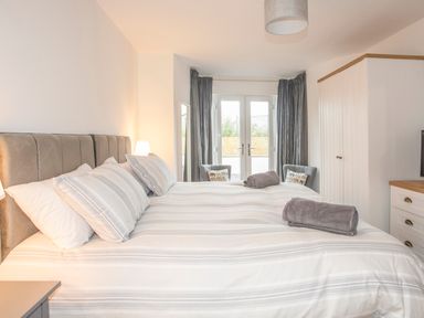 A bedroom with a large bed two gray chairs a wardrobe and a chest of drawers at Cambrian House in Criccieth