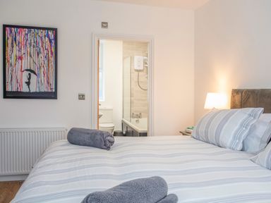 A bedroom with a striped bedspread and pillows towels on the bed a lamp on the nightstand and a bathroom visible through an open door at Cambrian House in Criccieth