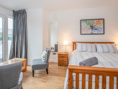 A bedroom with a wooden bed with striped bedding a bedside table with a lamp two gray chairs and a wooden table at Cambrian House in Criccieth
