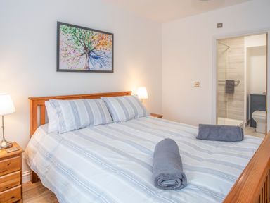 A bedroom with a wooden bed and striped bedding and an ensuite bathroom at Cambrian House in Criccieth