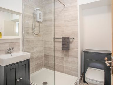 A bathroom with a shower area a sink with cabinet and a toilet at Cambrian House in Criccieth