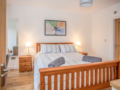 A bedroom with a wooden bed frame two bedside tables with lamps and a painting above the bed at Cambrian House in Criccieth