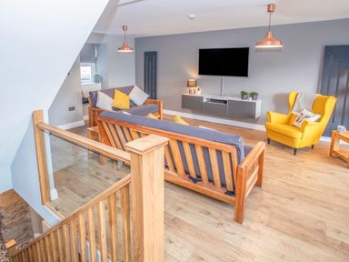 A living room with wooden sofas yellow armchair and wall mounted television at Cambrian House in Criccieth