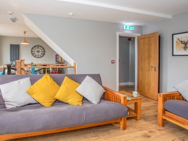 A sitting area with wooden framed sofas with cushions next to an open wooden door and a dining area in the background at Cambrian House in Criccieth