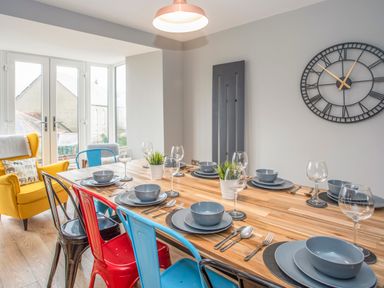 A dining room with a wooden table set for eight with colored metal chairs and a yellow armchair at Cambrian House in Criccieth
