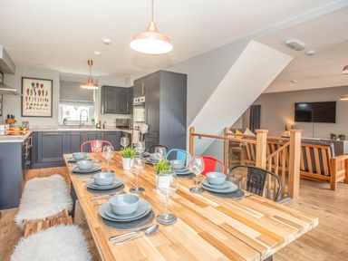 A kitchen and dining area with a wooden table set for eight and an open living room at Cambrian House in Criccieth