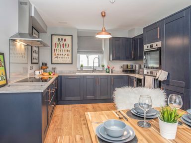 A kitchen with navy blue cabinets a wooden dining table set with grey dishes and wine glasses at Cambrian House in Criccieth