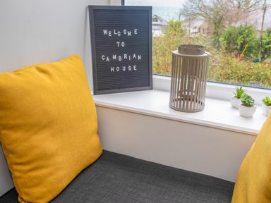 A seating area with yellow cushions near a window with a sign saying welcome to cambrian house a lantern and small potted plants on the windowsill at Cambrian House in Criccieth