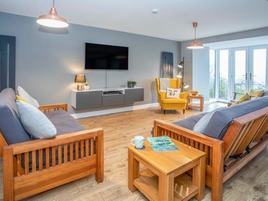 A living room with wooden sofas a yellow armchair a wall-mounted TV and a wooden coffee table at Cambrian House in Criccieth