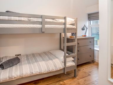 A bedroom with a gray bunk bed and a gray chest of drawers by a window at Cambrian House in Criccieth