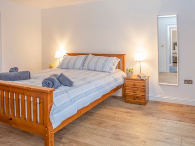 A bedroom with a wooden bed with striped bedding and gray towels two bedside tables with lamps and plants a wall mirror and wooden flooring at Cambrian House in Criccieth