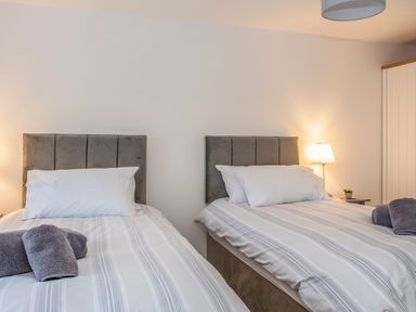 A bedroom with two beds with white and gray striped bedding and gray towels at Cambrian House in Criccieth