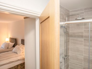 A view of a bedroom with two beds and a bedside lamp next to a bathroom with a shower at Cambrian House in Criccieth