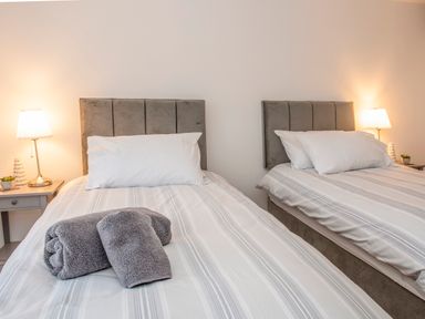A bedroom with two single beds with striped bedding and pillows and lamps on bedside tables at Cambrian House in Criccieth