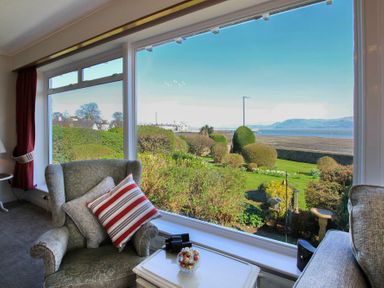 A living room with armchairs and a small table looking out to a garden and sea view at Camlan in Beaumaris