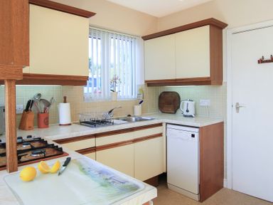 A kitchen with beige cabinets a gas stove a sink dishwasher kettle and a cutting board with lemons at Camlan in Beaumaris