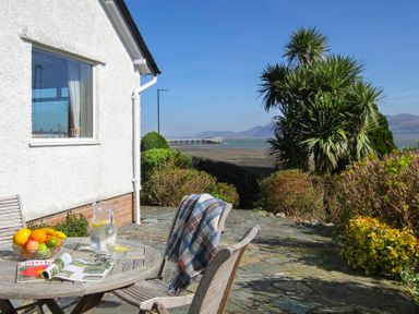 A patio with wooden table and chairs and a sea view at Camlan in Beaumaris