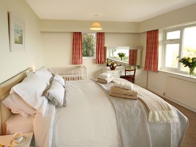A bedroom with a bed folded towels on it a crib a dressing table with a chair and flowers at Camlan in Beaumaris