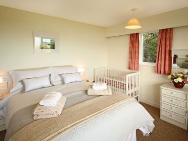 A bedroom with a double bed a crib a dresser with flowers and a window with curtains at Camlan in Beaumaris