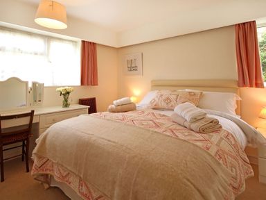 A bedroom with a bed covered with beige and patterned bedding a desk with a chair and a vase of flowers at Camlan in Beaumaris