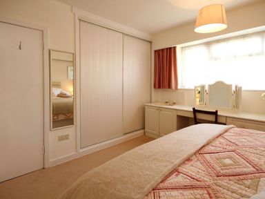 A bedroom with a bed covered in a quilt next to a built in wardrobe and a dressing table with a chair at Camlan in Beaumaris