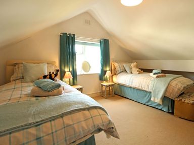 A bedroom with two single beds bedside tables lamps and a window with curtains at Camlan in Beaumaris