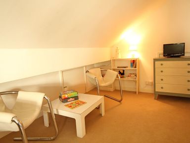 A room with two modern chairs a small table with board games a dresser with a tv and a bookshelf with a lamp at Camlan in Beaumaris