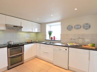 A kitchen with white cabinets a dishwasher an oven and a window with flowers on the sill at Cefn Isaf in Porthmadog