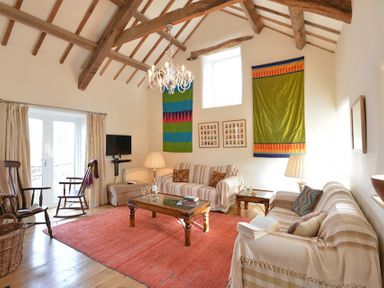 A living room with wooden beams on the ceiling sofas a coffee table and a red rug at Cefn Isaf in Porthmadog