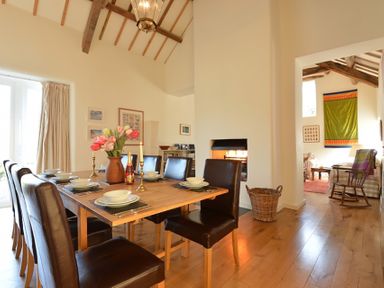 A dining room with a wooden table set with plates bowls candlesticks and flowers next to a fireplace and a sitting area visible through an open doorway at Cefn Isaf in Porthmadog