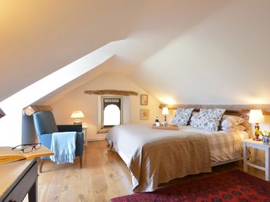 A bedroom with a bed pillows lamps an armchair small tables and wooden floor at Cefn Isaf in Porthmadog