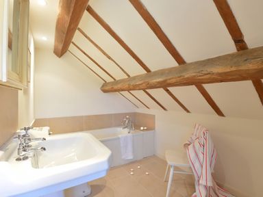 A bathroom with a sink and bathtub under a slanted ceiling with wooden beams at Cefn Isaf in Porthmadog