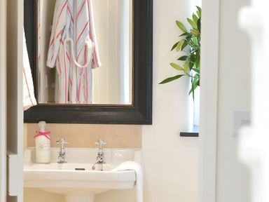 A bathroom sink with faucets a bottle a towel and a mirror reflecting a striped bathrobe with a plant on the windowsill at Cefn Isaf in Porthmadog