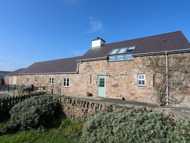 A stone cottage with a slate roof and garden in front at Tan Twr - Chellow Cottage in Dwyran