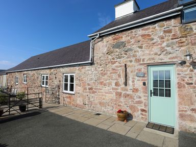Stone cottage exterior with light green door and windows with flower pot at Tan Twr - Chellow Cottage in Dwyran