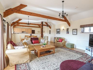A living room with beige sofas wooden coffee table dining area and exposed wooden beams at Tan Twr - Chellow Cottage in Dwyran