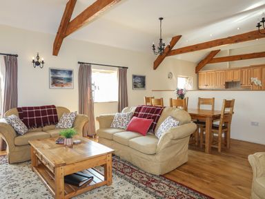 A living room with two beige sofas a wooden coffee table and dining table under wooden beams at Tan Twr - Chellow Cottage in Dwyran