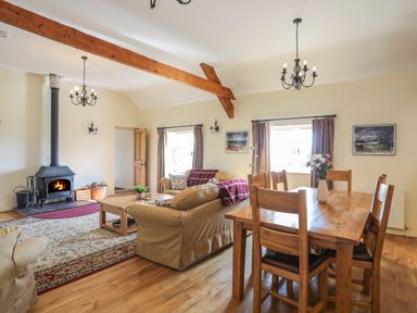 A living room with wooden dining table and chairs sofas and fireplace at Tan Twr - Chellow Cottage in Dwyran
