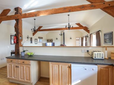 A kitchen countertop with wooden cabinets a toaster and exposed wooden beams at Tan Twr - Chellow Cottage in Dwyran