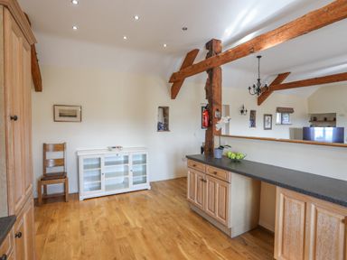A kitchen area with wooden cabinets a black countertop a wooden chair and a white cabinet at Tan Twr - Chellow Cottage in Dwyran