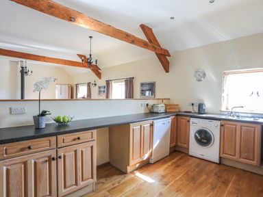 A kitchen with wooden cabinets a dishwasher a washing machine and a sink at Tan Twr - Chellow Cottage in Dwyran